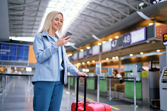 Travel and technology. Online check-in. Female traveler using smartphone waiting for boarding near registration desk line.