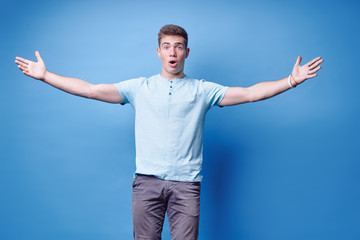 Fototapeta premium It is so big. Colorful studio portrait of young man showing big size with his hands. Blue background.