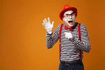 Naklejka premium Happy mime man in red hat, white gloves and striped t-shirt on blank orange background