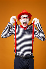 Happy mime looking at camera in vest and red hat Isolated on orange background