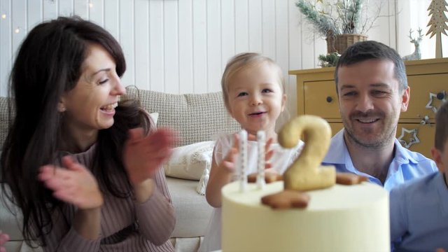 Cute little child girl is blowing the candles on birthday cake. Family is celebrating birthday of two years daughter