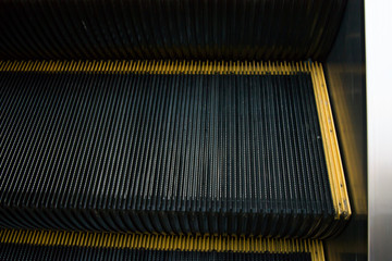 One escalator step with a yellow cant. Close-up, dark photo.