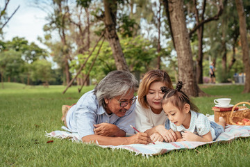 Grandmother,Grandfather and grand daughter enjoying sunny garden holiday together, outdoors space, leisure lifestyle,happy teaching with flare light sky in park.