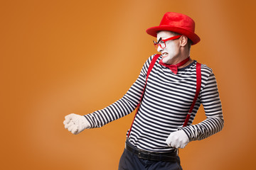 Dissatisfied mime man in vest and red hat on orange background