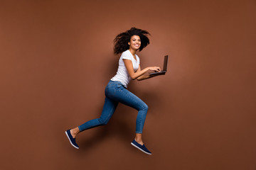 Fototapeta na wymiar Full body photo of funny dark skin lady jumping high holding notebook running writing email at same time wear casual white t-shirt jeans isolated brown color background