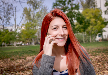 Happy redhead woman talking on the phone outdoors.