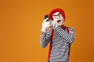 Fototapeta na wymiar Mime man in white gloves and red hat takes selfie on orange background