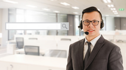 Asian smart businessman customer support phone operator in office space interior background with blank search bar graphic.Concept of business using technology.