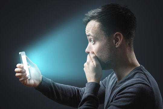 Appalled man looking at his glowing smartphone screen