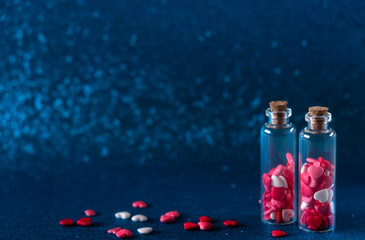 Two glass bottles with heart-shaped sugar sprinkles On gliter blue background. Valentines day concept, sweet love.
