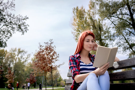 Young Woman Resting On Park Bench And Reading A Book.