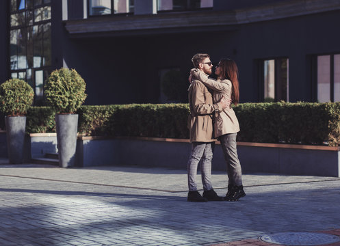 Young fashion stylish couple in checkered pants and coat hugging on streets of city
