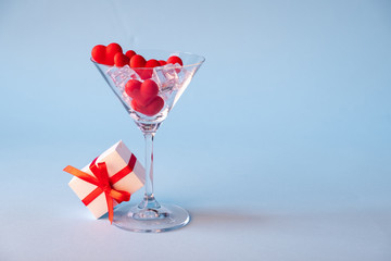 Glass with red heart shaped sugar candy and ice and gift box a blue background. Time for love.Valentines Day, anniversary or wedding celebration concept. Copy space.