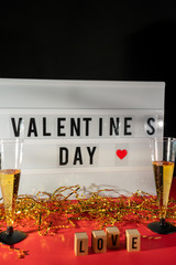 Bright Valentine's Day sign, champagne glasses and gold confetti.