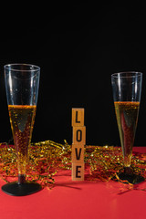 Two sparkling champagne glasses, with gold confetti and red background with wooden pieces with the message love.