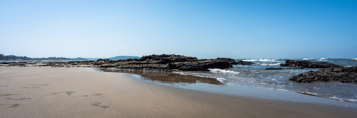 Panoramic view of the Arabian sea coast in India. Long sandy beach with footprints background. Large boulders on the shore. Surf Waves breaking on the rocks. Horizon line of the ocean. Header. 