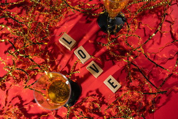 Two sparkling champagne glasses, with gold confetti and red background with wooden pieces with the message love.