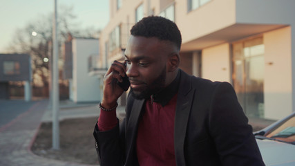 Happy young african american man stand speak use phone in city near white car technology...
