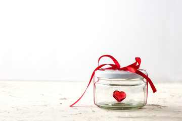 Little red heart in glass jar with ribbon on white background