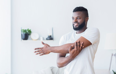 Young black man training and stretching arm at home