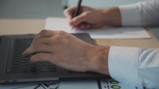 business man hands with using laptop to work and writing on paper with a pen. slow motion. Business financial, trade stock maket and social network concept. closeup. ux design concept.