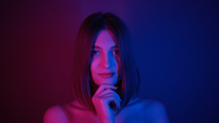 Seductive young woman with straight hair looking at camera, dancing. Magical power of femininity.Charismatic. Neon lighting. Shooting, footage. Style, fashion