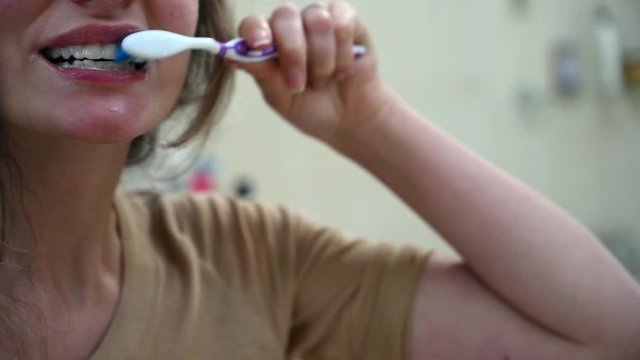 Woman brushing her white teeth with a purple brush, close up