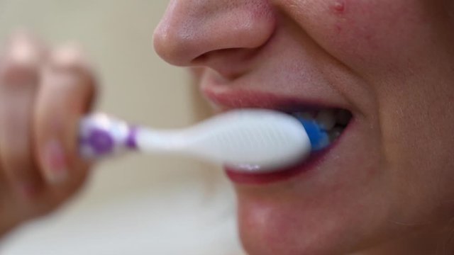 Woman brushing her white teeth with a purple brush, close up