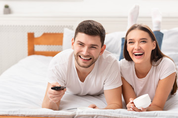 Happy Couple Watching TV Lying In Bed Indoor