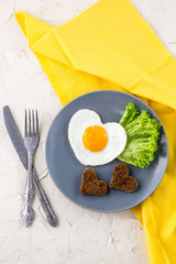 Valentines day breakfast with heart shaped fried eggs served on grey plate and yellow napkin