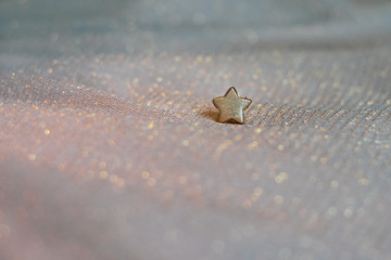 kleiner goldener Stern auf glitzerndem Stoff in Pastelltönen, der märchenhaft und magisch wirkt