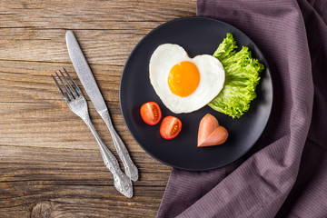 Valentines day breakfast with heart shaped fried eggs served on grey plate.