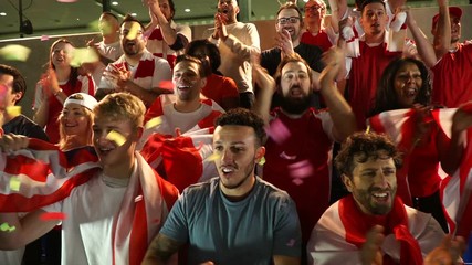 Football / Soccer fans or supporters in stadium celebrate with confetti falling. They jump and cheer. Super slow motion. Red. Stock Video Clip Footage