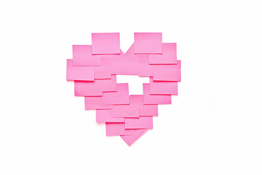 Blank pink sticky notes sticked on white wall in heart shape
