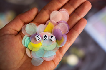 A person holds colourful pastel confetti in their hands, on which the word Yay is written in little letters, Concept of Joy, Happiness, Party