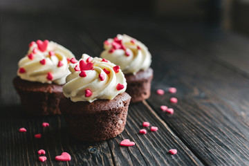 Valentine cupcakes, decorated with sweet hearts on dark wooden table.