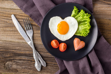 Valentines day breakfast with heart shaped fried eggs served on grey plate.
