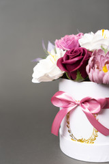Flowers in bloom: multi-colored red and pink buds in a white round box on a grey background.
