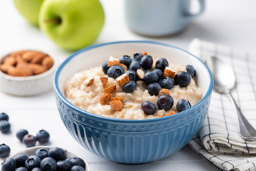 Oatmeal porridge bowl with blueberries and almonds in blue bowl. Healthy breakfast food, vegetarian breakfast high in fiber and slow carbs - obrazy, fototapety, plakaty