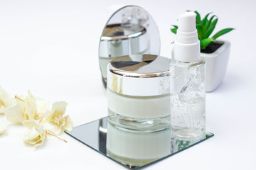 Cosmetic bottles with serum, gel, face cream on a mirror a white background with a flower. Skin...