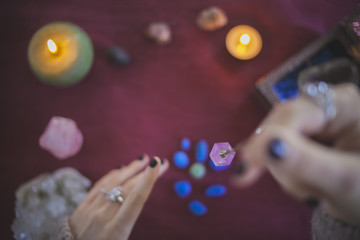 Young woman catching an amethyst pendulum with an esoteric and mystical background of candles, stones and crystals