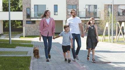 Cheerful family with kids playing with their dog outdoors in the playfround. Handsome man father throwing a ball to the puppy teaching him commands.