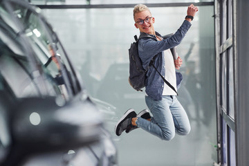 Happy hipster guy jumping indoors against grey background and near car