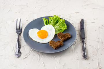 Valentines day breakfast with heart shaped fried eggs served on grey plate