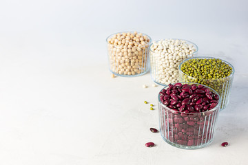 Bowls of various legumes: chickpeas, lentils, mung, red and white bean on a gray background.