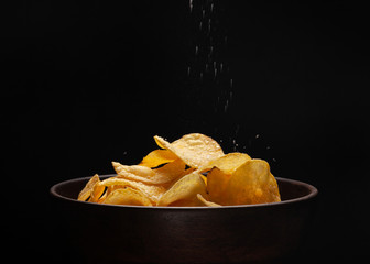 Сhips in a wooden bowl on a dark background sprinkled with salt
