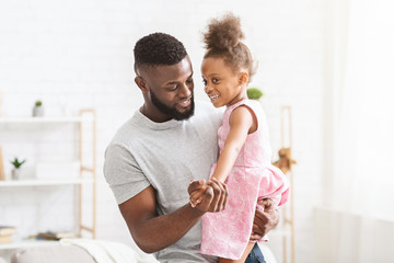Young black father holding little daughter, dancing together