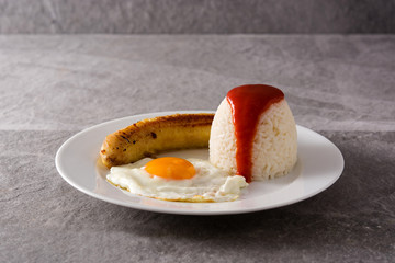 Arroz a la cubana Typical Cuban rice with fried banana and fried egg on gray background	