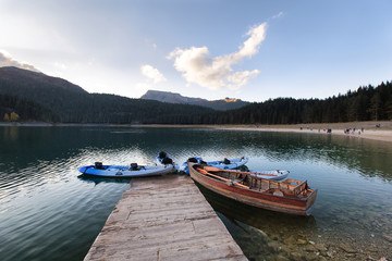 Mountain lake sunrise landscape.Old wooden boat and blue kayaks at the plank. Lake reflection. Pine forest background.