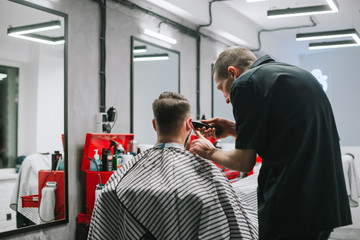 A professional barber cuts the client's haircut in a comfortable, modern barber shop. Male hairdresser with a haircut in his hands creates a stylish hairstyle for a man.Barbershop.